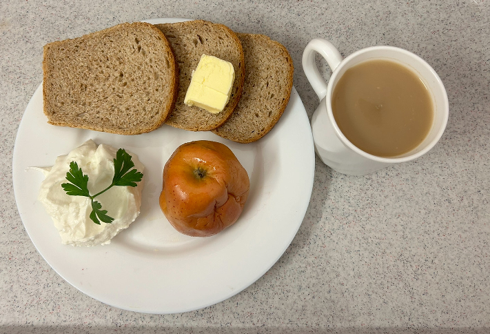 Na zdjęciu znajduje się: Kawa zbożowa z mlekiem, Chleb graham, Masło extra 82%, Serek homo naturalny, Jabłko pieczone